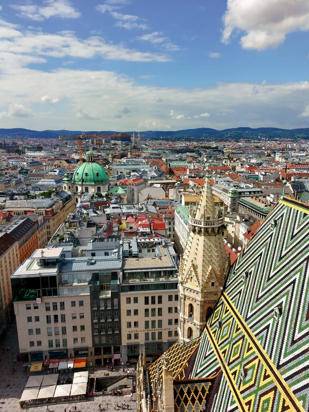 A panoramic view of Vienna. The colorful, mosaic roof of St. Stephen's Cathedral is visible, along with many buildings of the city.